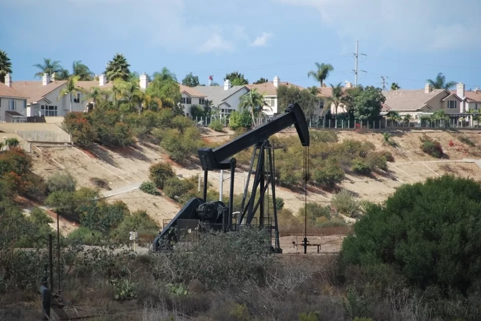 Black pumpjack oil derrick with houses in background